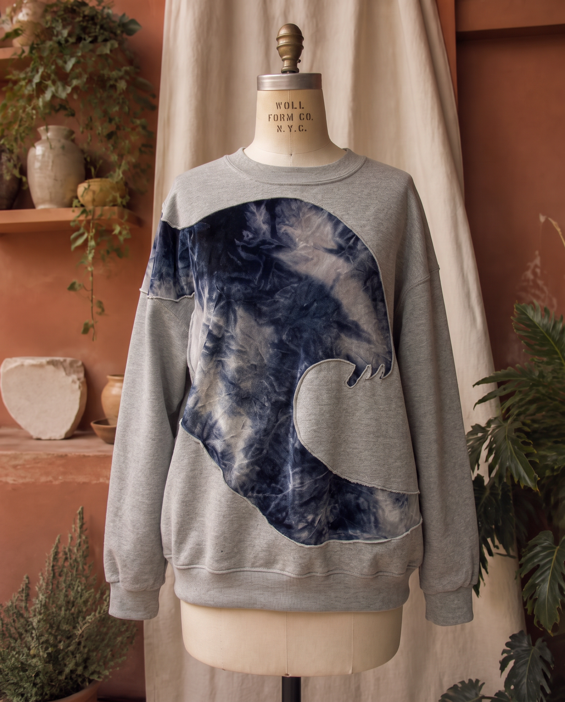Upcycled gray sweatshirt with a wave-shaped cutout revealing navy tie-dye velvet, on a dress form